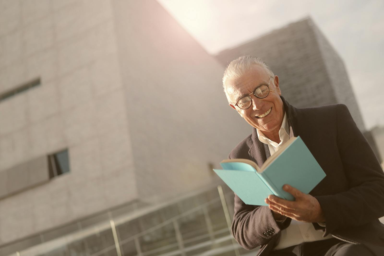 Smiling senior man enjoying reading a book outdoors on a sunny day.